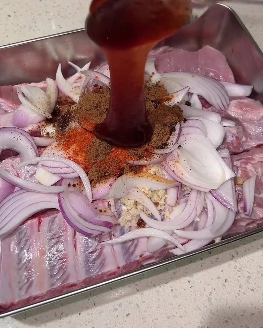 돼지갈비, 양파, 마른 향신료가 쌓인 위로 진한 붉은색 차슈 소스를 붓는 모습.