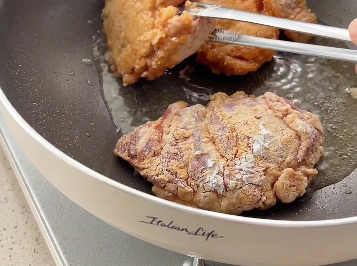 프라이팬에서 집게로 닭고기를 뒤집으며 노릇하고 바삭한 크러스트를 보여주는 모습.