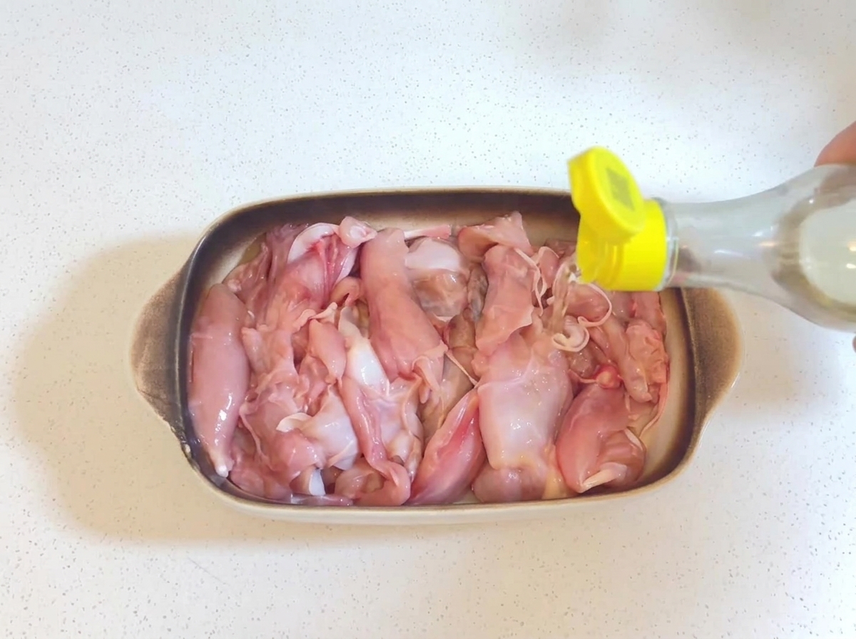 노란색 뚜껑이 달린 작은 병에서 베이킹 디쉬 속 생닭고기로 투명한 맛술을 붓는 모습.