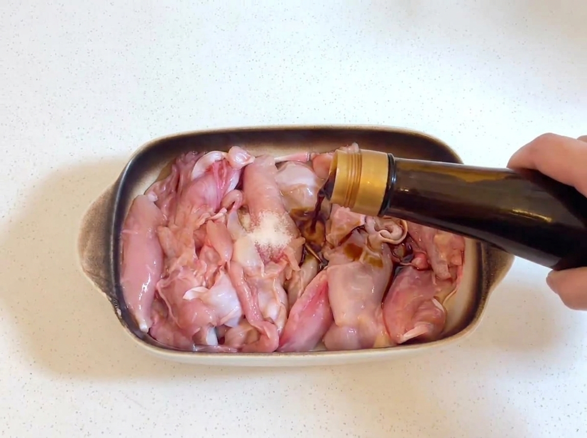 유리병에서 생닭고기 위로 진간장을 붓고 있으며, 닭고기 위에 작은 소금 알갱이가 보이는 모습.