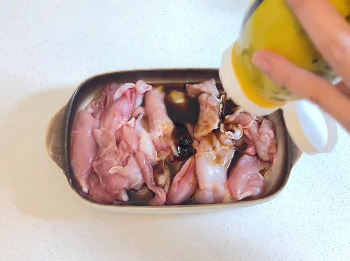 간장 양념에 담겨 있는 생닭고기 위로 노란색 용기에서 진한 굴소스가 짜내어지는 모습.