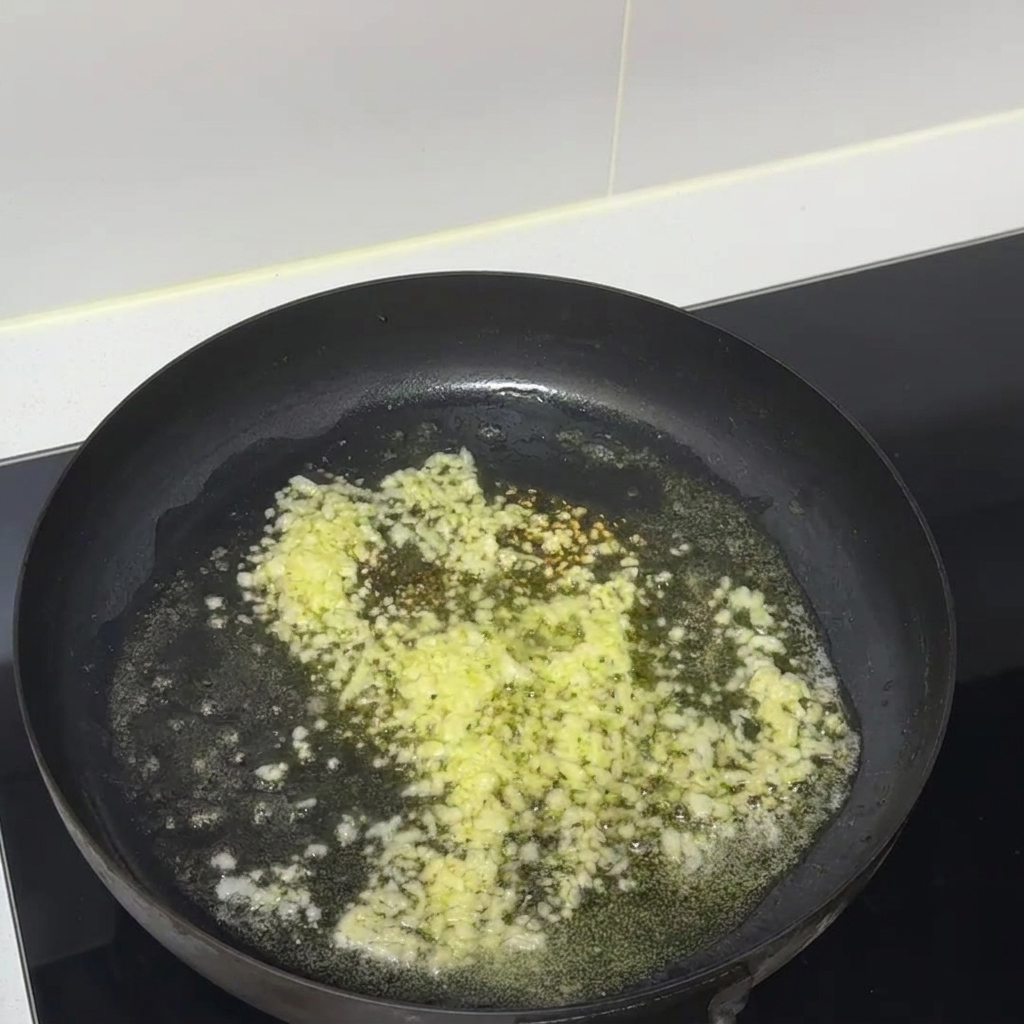 검은색 논스틱 프라이팬에서 다진 마늘과 녹은 버터가 함께 지글지글 끓고 있는 모습.