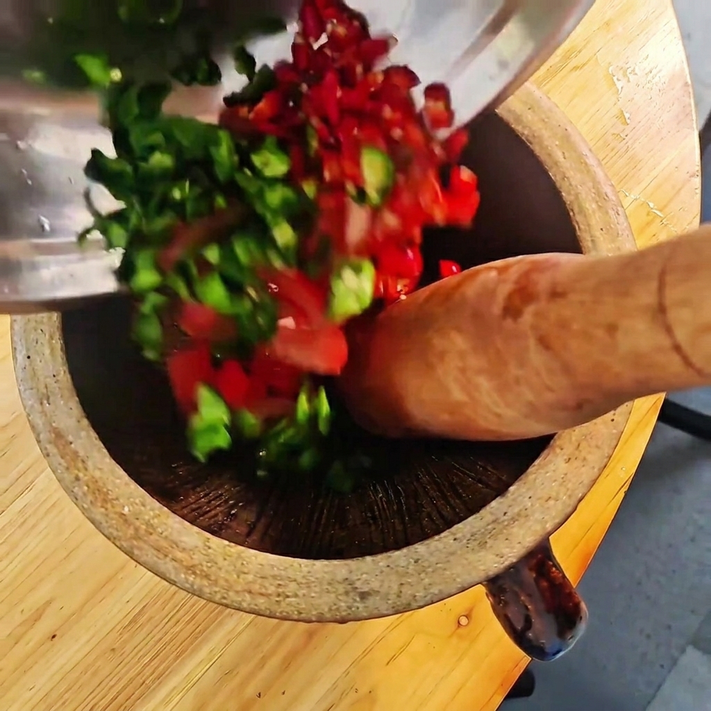 나무 절구에 다진 청양고추, 홍고추, 토마토를 넣고 공이로 찧는 모습.