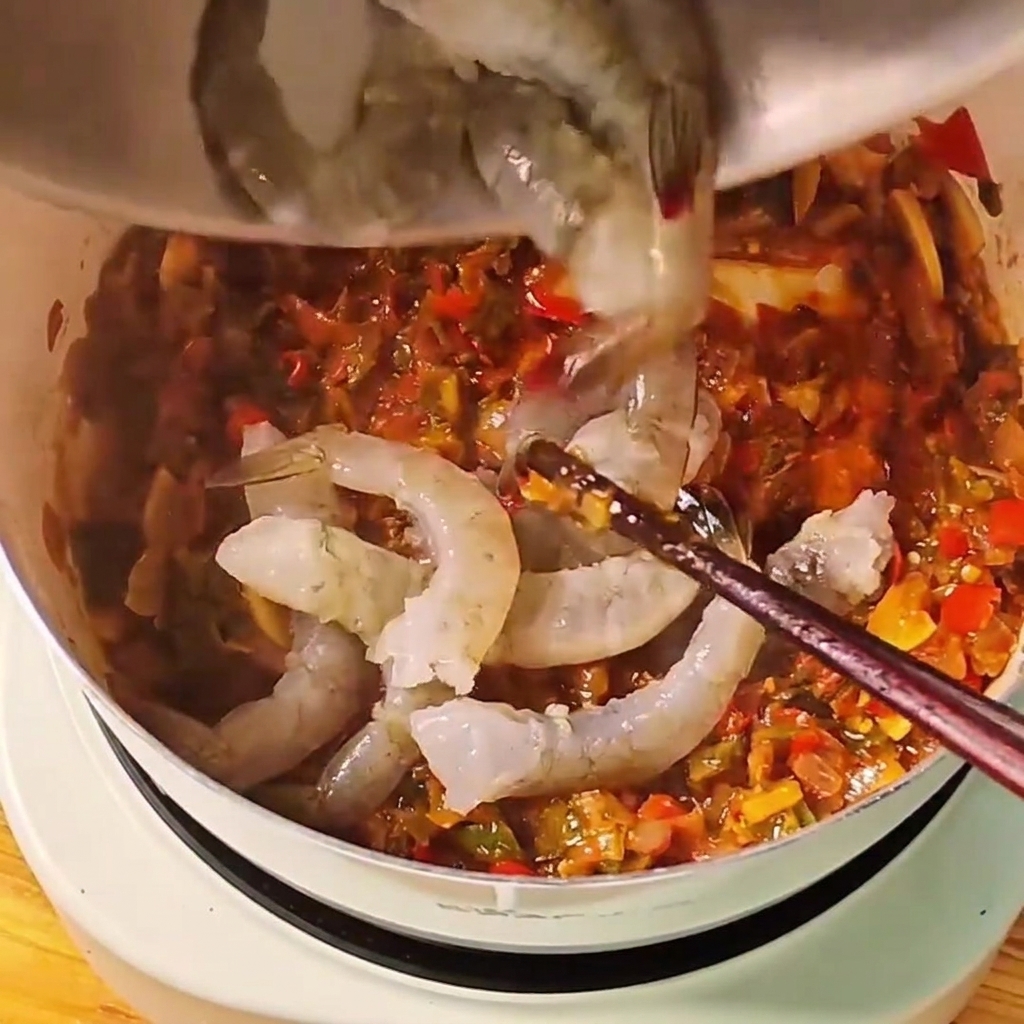 끓고 있는 붉은 토마토소스 냄비에 회색빛 생새우를 넣는 모습.