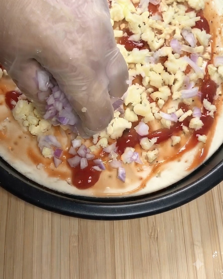 투명 장갑을 낀 손으로 토마토소스가 발린 피자 베이스 위에 다진 적양파와 모짜렐라 치즈를 뿌리는 모습.