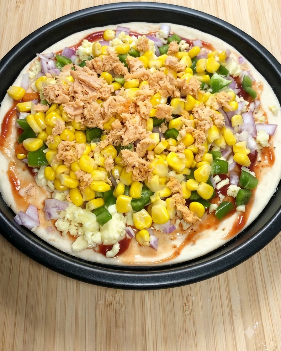 토마토소스, 모짜렐라, 청피망, 스위트콘, 그리고 조각난 통조림 연어가 토핑된 둥근 피자 베이스.