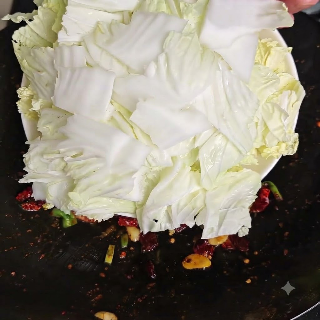 흰 접시에 담긴 신선하게 썬 생배추 조각들을 달궈진 웍 안으로 털어 넣는 모습.