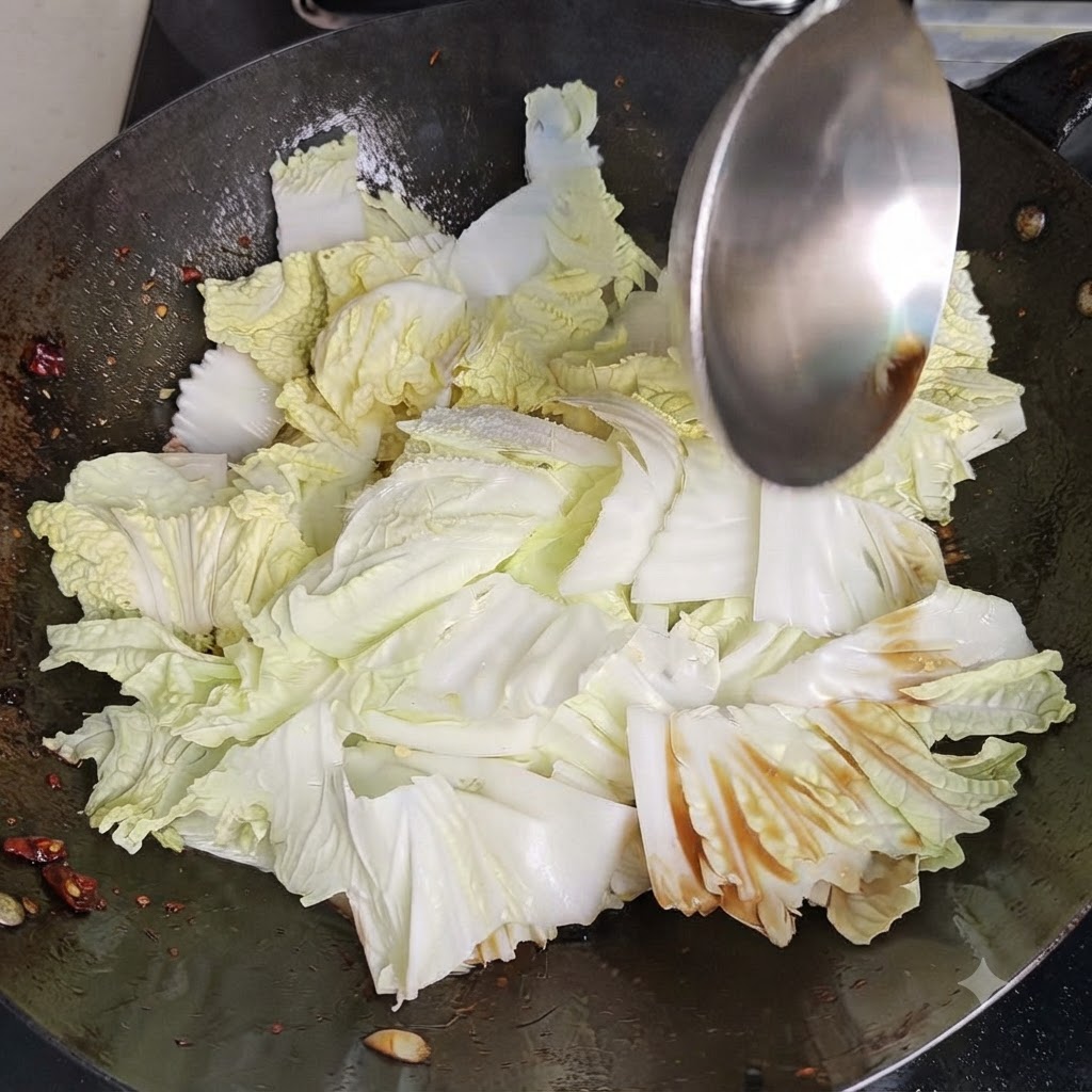 금속 웍 뒤집개로 뜨거운 웍 안에서 배추와 양념을 힘차게 볶고 섞어주는 모습.