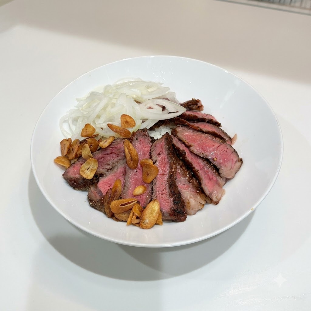 밥 위에 썬 스테이크, 양파, 노릇한 황금빛 바삭한 마늘칩이 흩뿌려진 흰 그릇.