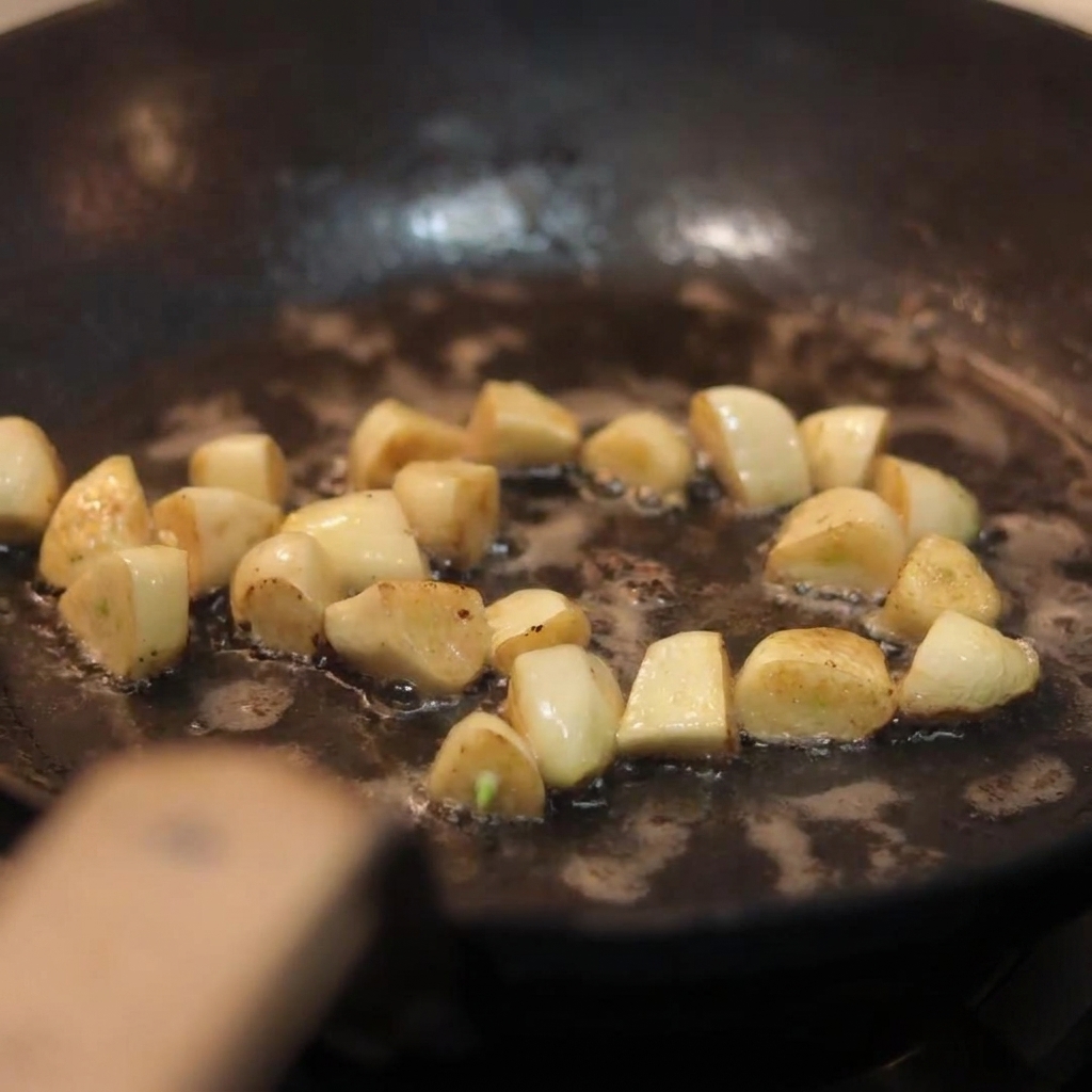 노릇하게 볶아진 마늘이 있는 팬에 슬라이스한 양송이 버섯을 넣는 모습.
