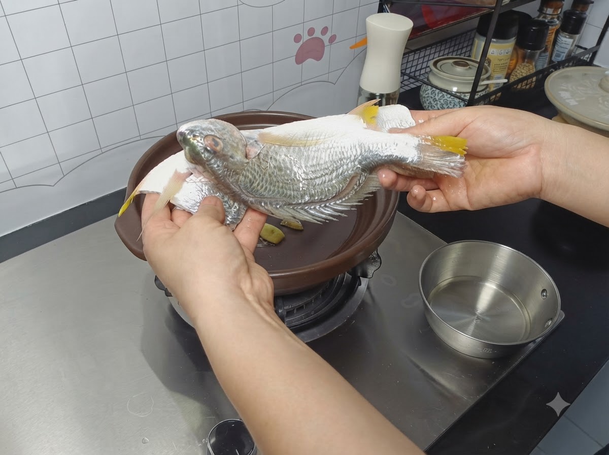 밑간을 한 통생선을 뚝배기 안의 생강 조각 위에 올리는 모습.