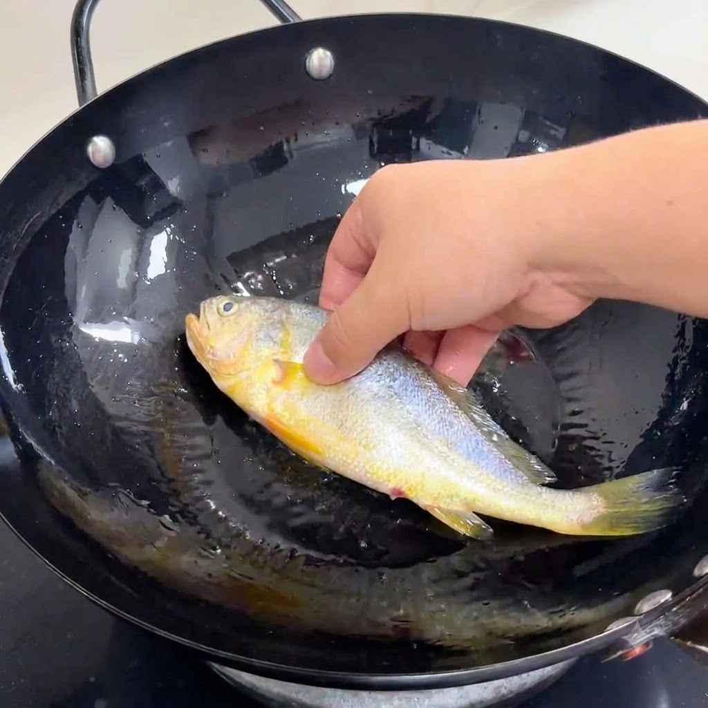 달궈진 식용유가 담긴 검은색 웍에 양념된 통생선을 손으로 조심스럽게 넣는 모습.