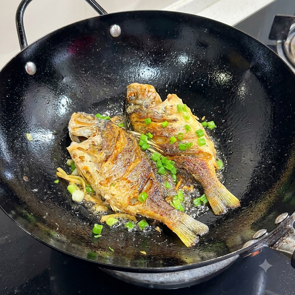 검은색 웍 안의 노릇하게 구워진 생선 위에 잘게 썬 파를 뿌리는 모습.
