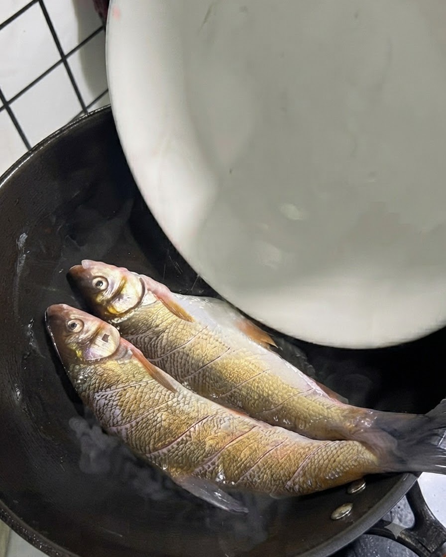 기름이 달궈진 핫 웍 안에 두 마리의 통생선이 놓여 있는 모습.