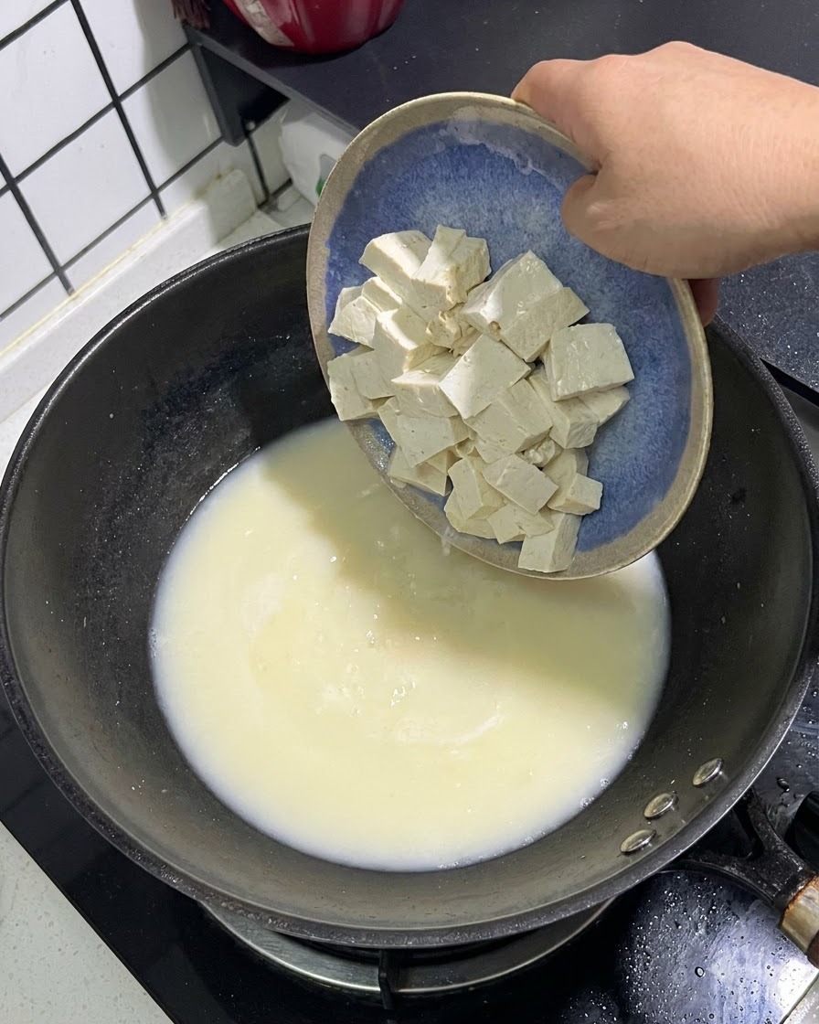 파란 접시에 담긴 하얀 두부 큐브가 크리미한 생선 육수 냄비 속으로 미끄러져 들어가는 모습.