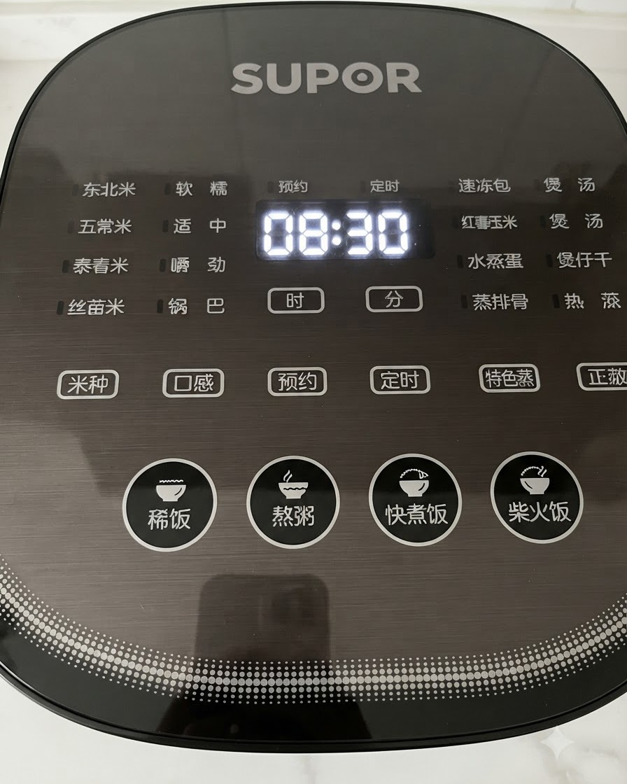 시간이 표시되는 검은색 디지털 밥솥 조작부의 버튼을 누르고 있는 손의 클로즈업 뷰.