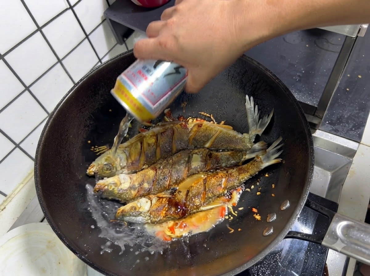 양념된 튀긴 생선과 볶은 향신료가 담긴 웍에 맥주 캔을 붓는 모습.