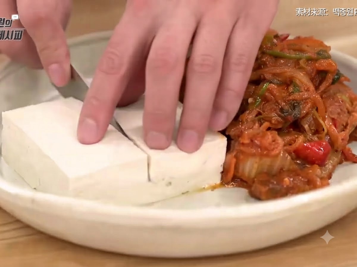 접시 위에서 새콤하게 볶은 김치와 돼지고기 옆에 데친 두부를 칼로 깔끔하게 써는 손.