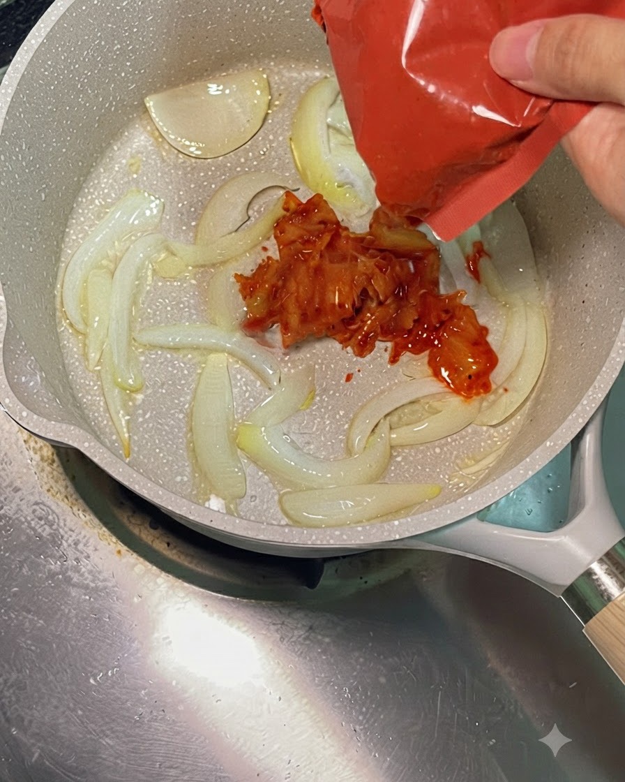 붉은색 포장지에서 썬 김치가 볶아진 양파가 있는 뜨거운 팬으로 바로 투입되는 모습.
