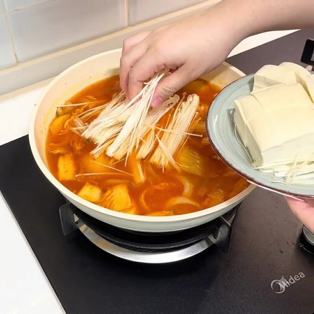 끓는 국물에 팽이버섯과 자른 두부를 넣는 모습.