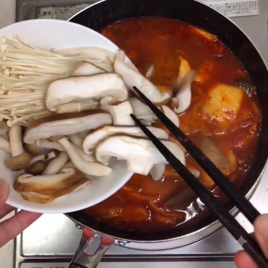 보글보글 끓는 찌개 냄비에 모둠 버섯과 팽이버섯을 넣는 모습.