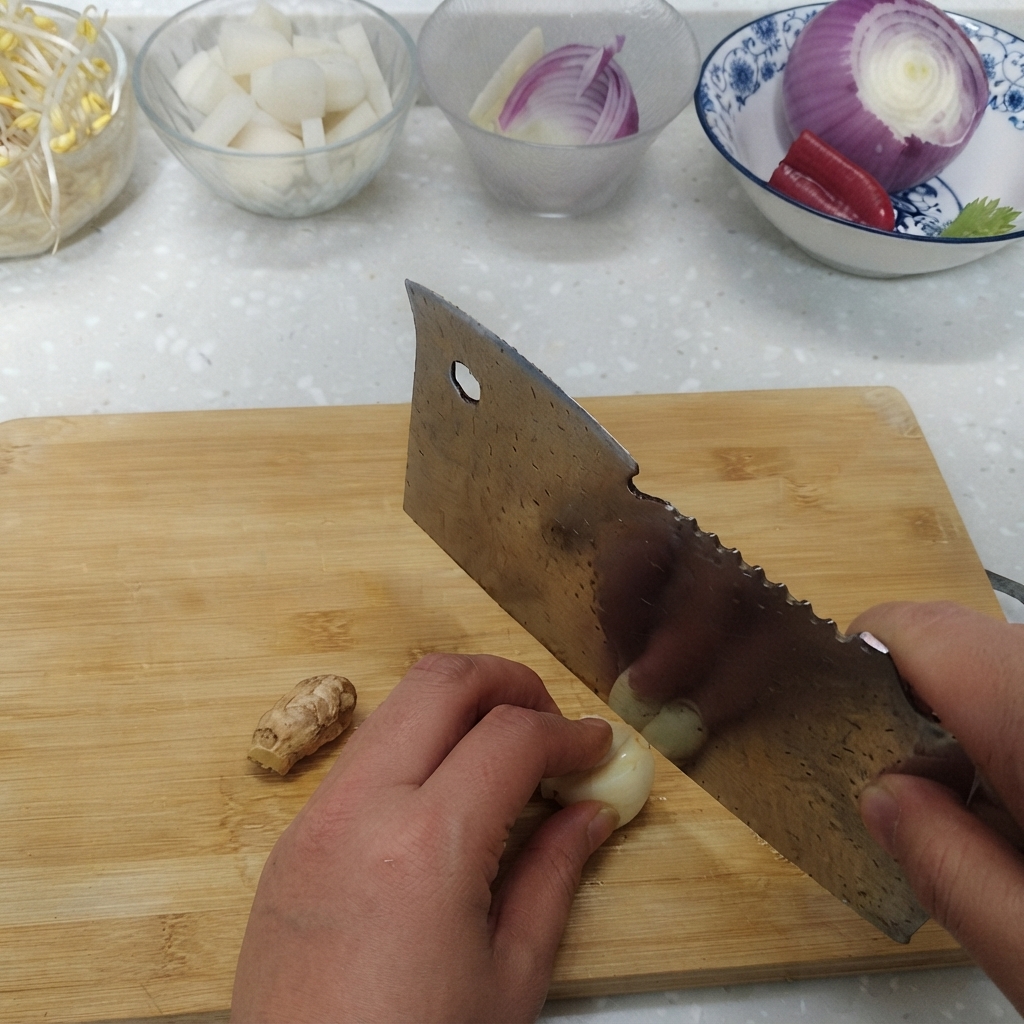 재료 그릇 옆 도마 위에서 마늘 쪽과 생강 뿌리를 얇게 썰고 있는 모습.