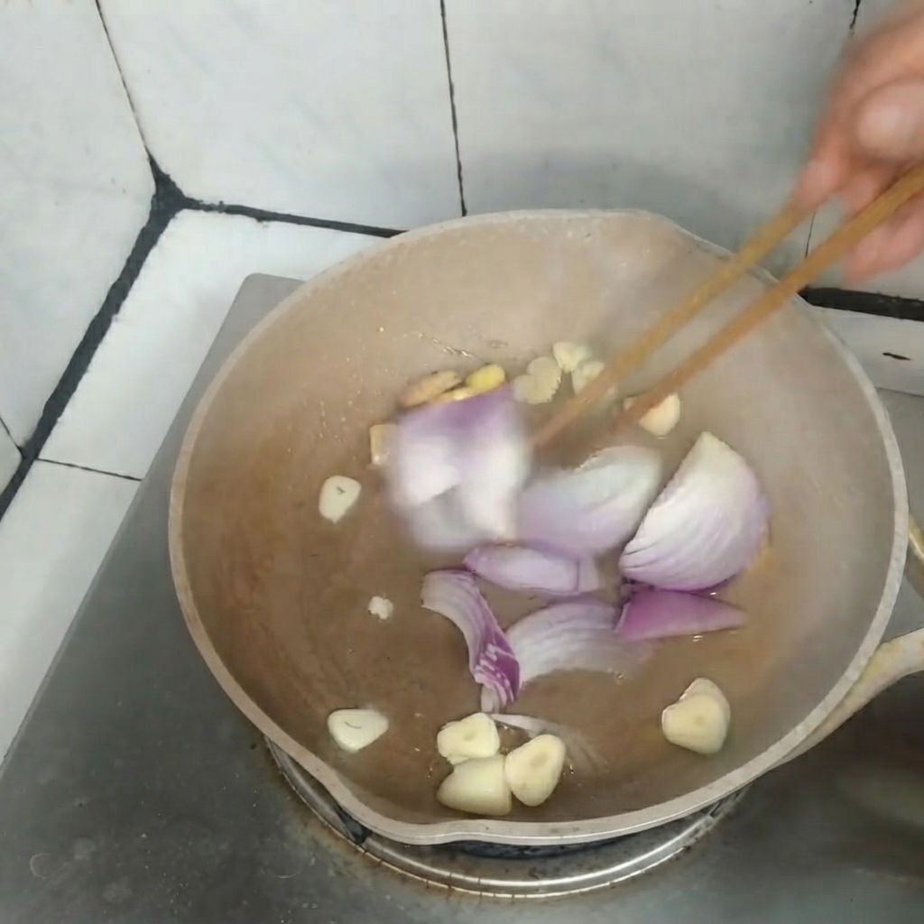 나무 젓가락을 이용해 팬에서 채 썬 적양파, 마늘, 생강을 함께 볶고 있는 모습.