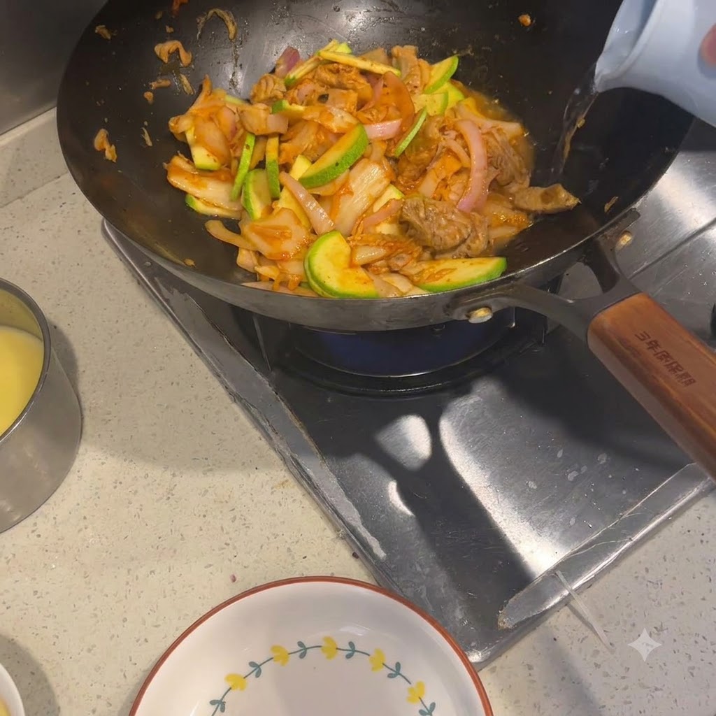 밝은 색상의 주전자에서 볶아진 재료가 담긴 웍으로 뜨거운 물이 부어지는 모습.