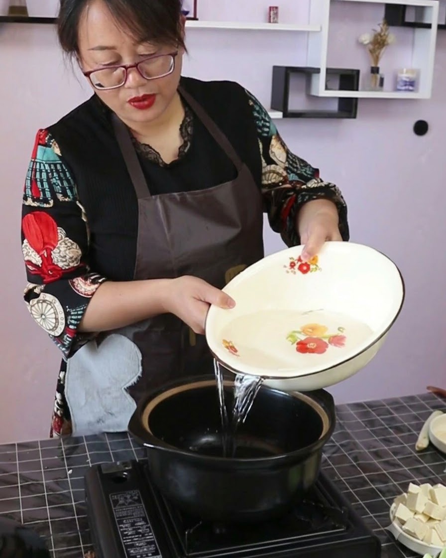 예쁜 그릇에 담긴 맑은 물을 휴대용 스토브 위의 검은색 도자기 냄비에 붓고 있는 모습.