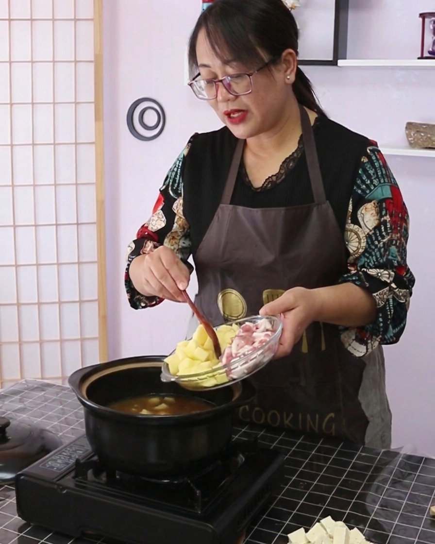 유리 접시에 담긴 깍둑썰기한 감자와 썬 삼겹살을 조리용 냄비에 털어 넣고 있는 모습.