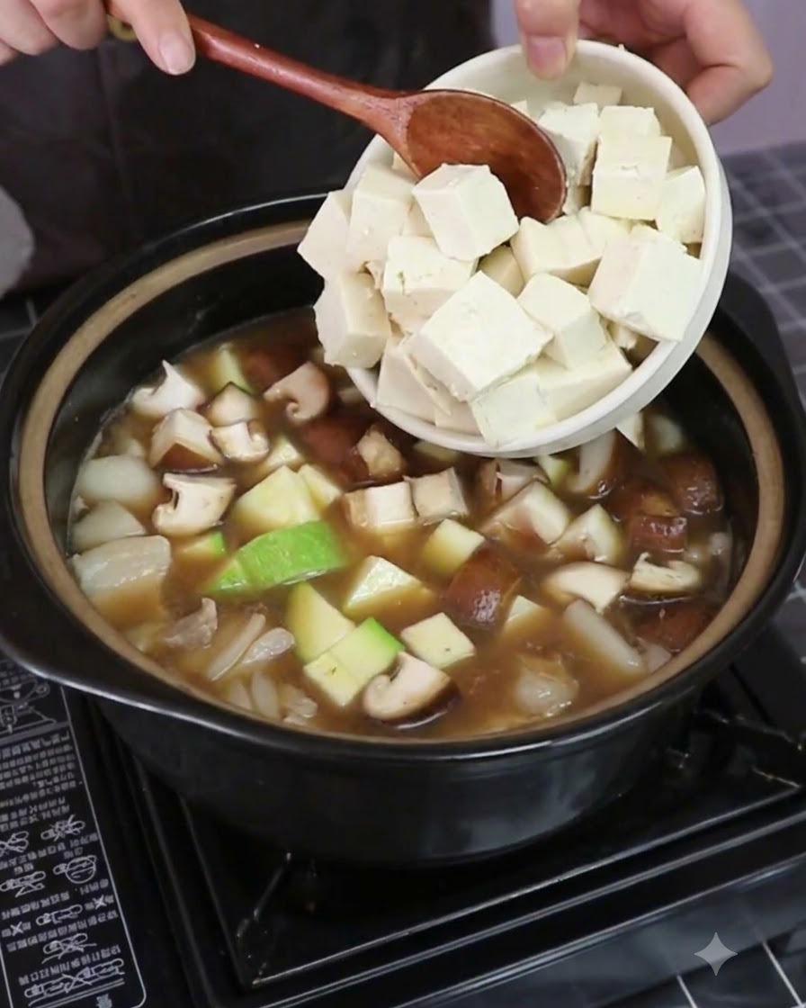 채소와 육수가 담긴 냄비에 염지된 단단한 두부 조각들을 넣고 있는 모습.