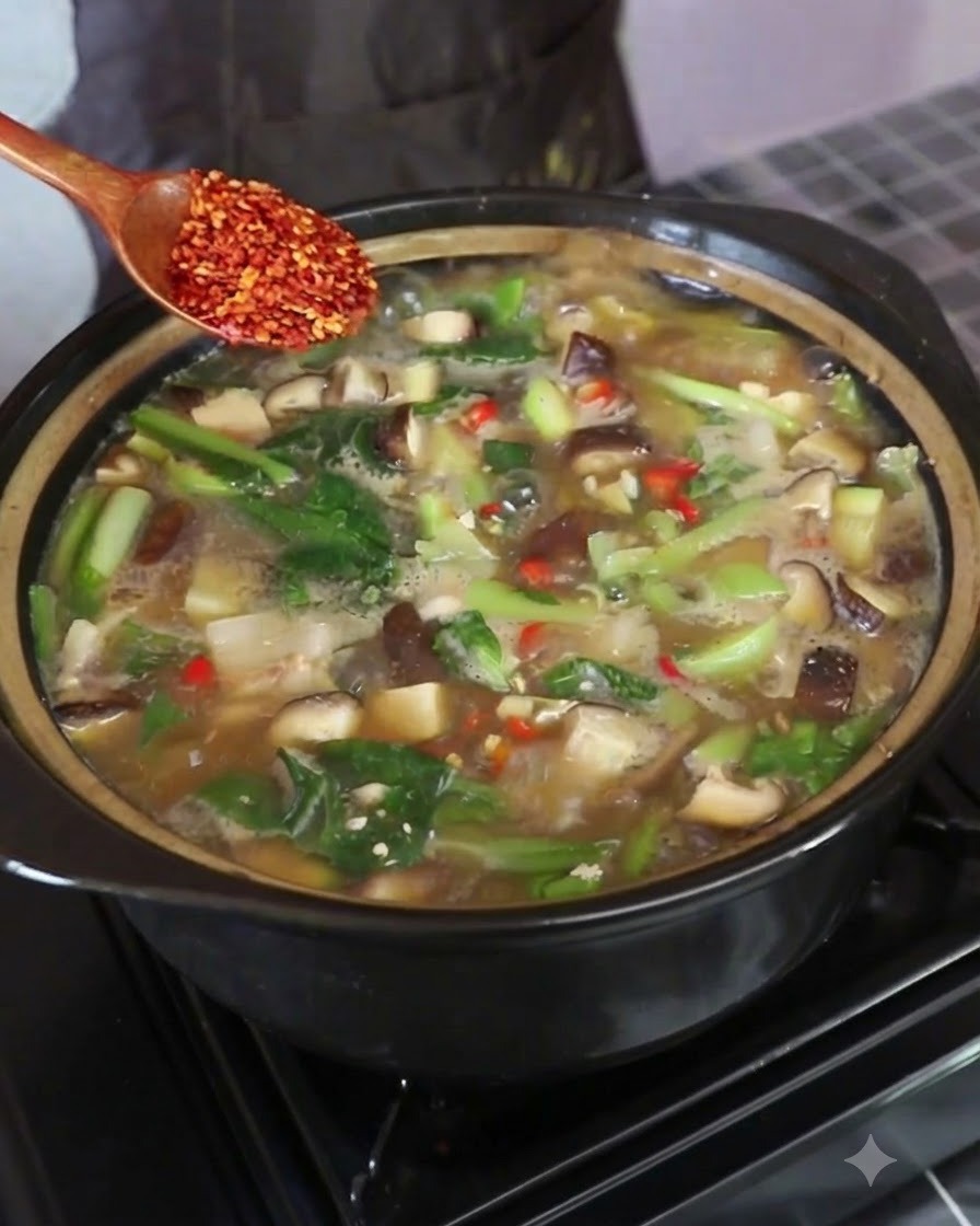 끓고 있는 찌개 냄비 위에서 나무 숟가락에 붉은 고추플레이크를 올려 저어주는 모습.