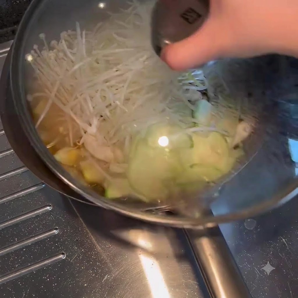채소와 육수가 보글보글 끓고 있는 프라이팬 위에 유리 뚜껑이 덮이는 모습