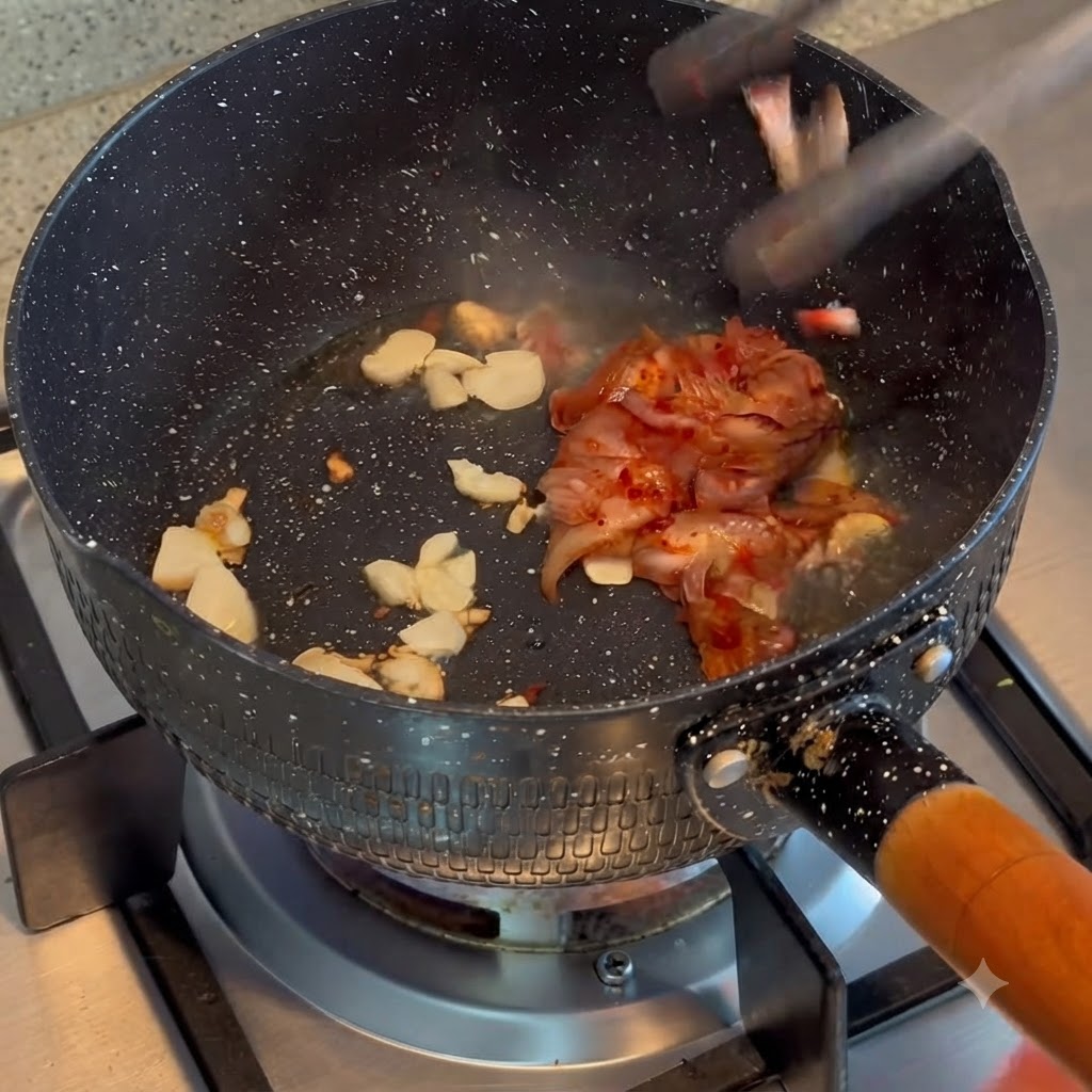 요리 냄비 안에서 볶아진 마늘과 김치가 함께 섞이며 볶아지는 모습.
