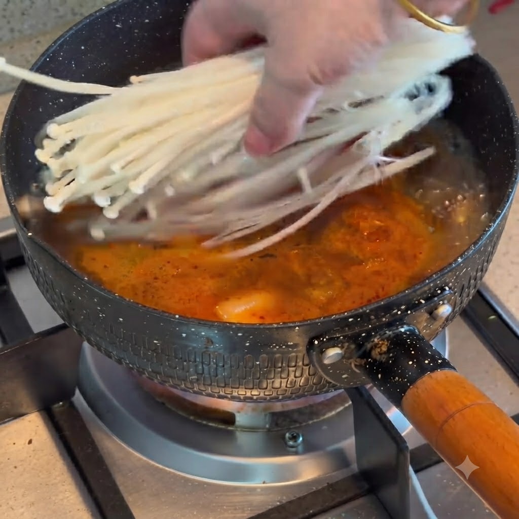 보글보글 끓는 김치와 소고기 스튜에 팽이버섯이 투입되는 모습.