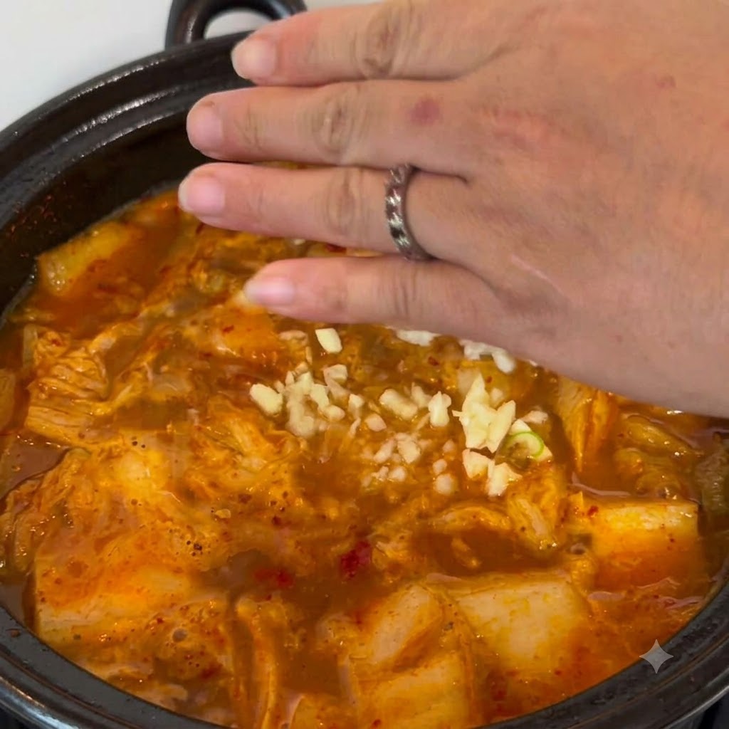 손으로 갓 다진 마늘을 보글보글 끓는 찌개 냄비 속으로 흩뿌려 넣는 모습.