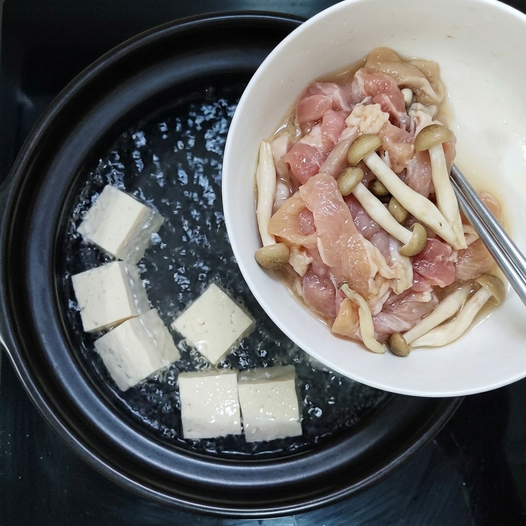 양념한 돼지고기와 생굴을 두부가 끓고 있는 냄비에 함께 넣는 모습.