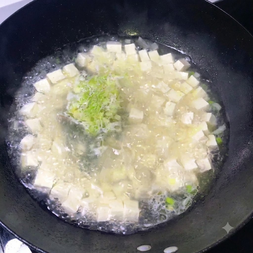 보글보글 끓고 있는 두부와 다진 파가 담긴 냄비에 양념을 뿌리는 모습.