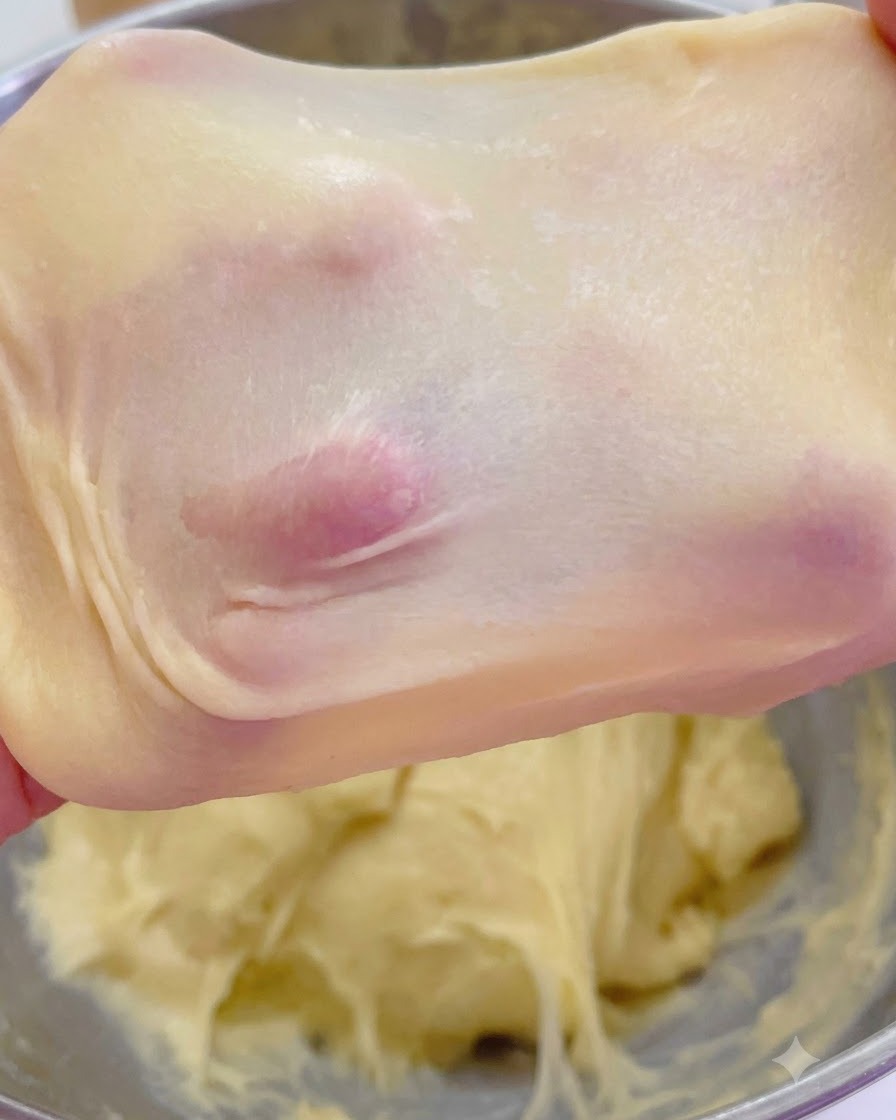 손가락으로 들어 올린 얇고 반투명한 창유리 막을 보여주는 늘어난 브리오슈 반죽.