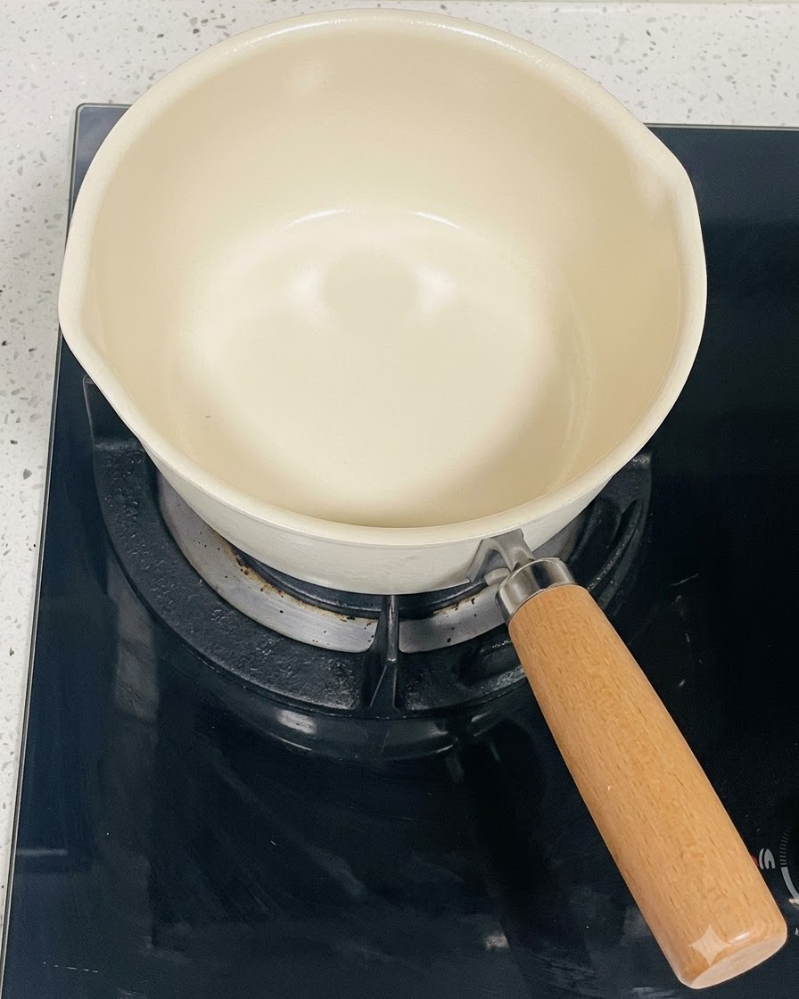 검은색 인덕션 버너 위에 놓여 있는 크림색의 빈 냄비.