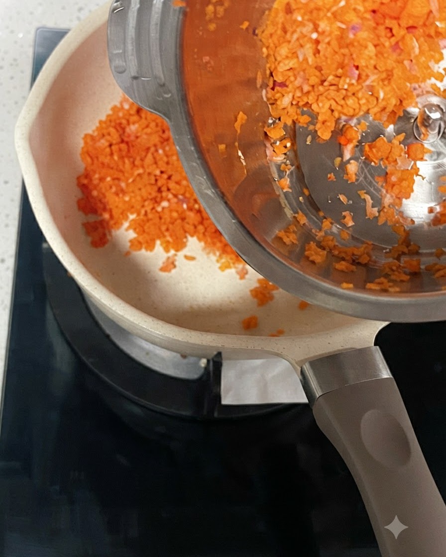 철제 용기에서 예열된 냄비로 잘게 다져진 당근과 양파가 쏟아져 들어가는 모습.