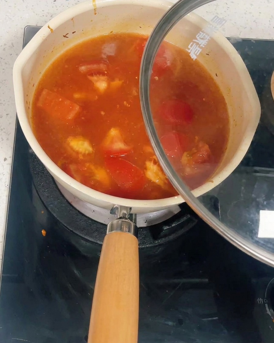 유리 뚜껑이 덮이고 있는 토마토 닭고기 소스로 가득 찬 냄비.