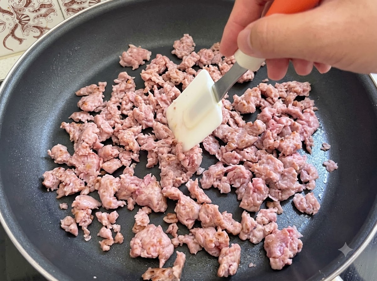 팬에서 주걱으로 이탈리안 소시지 미트를 적극적으로 저으며 볶고 있는 모습.