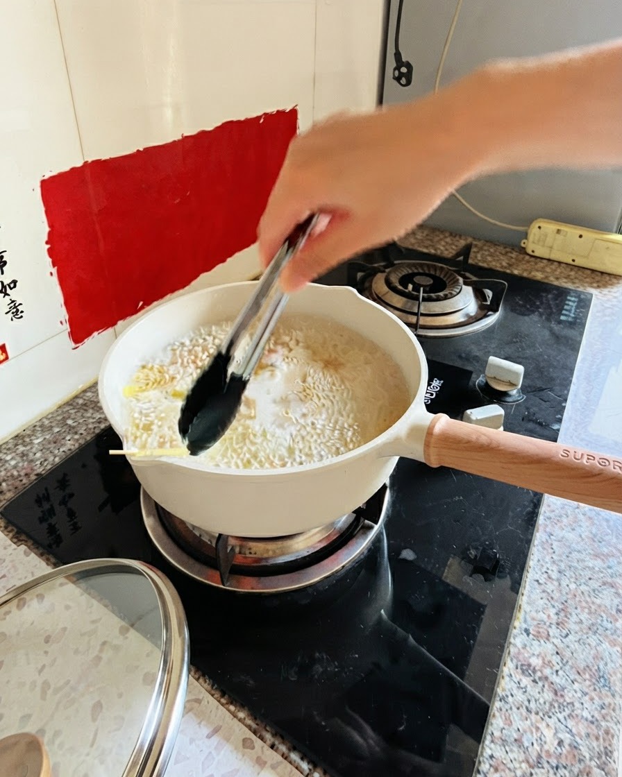 스토브 위 끓는 물과 파스타가 담긴 냄비를 집게로 젓는 모습
