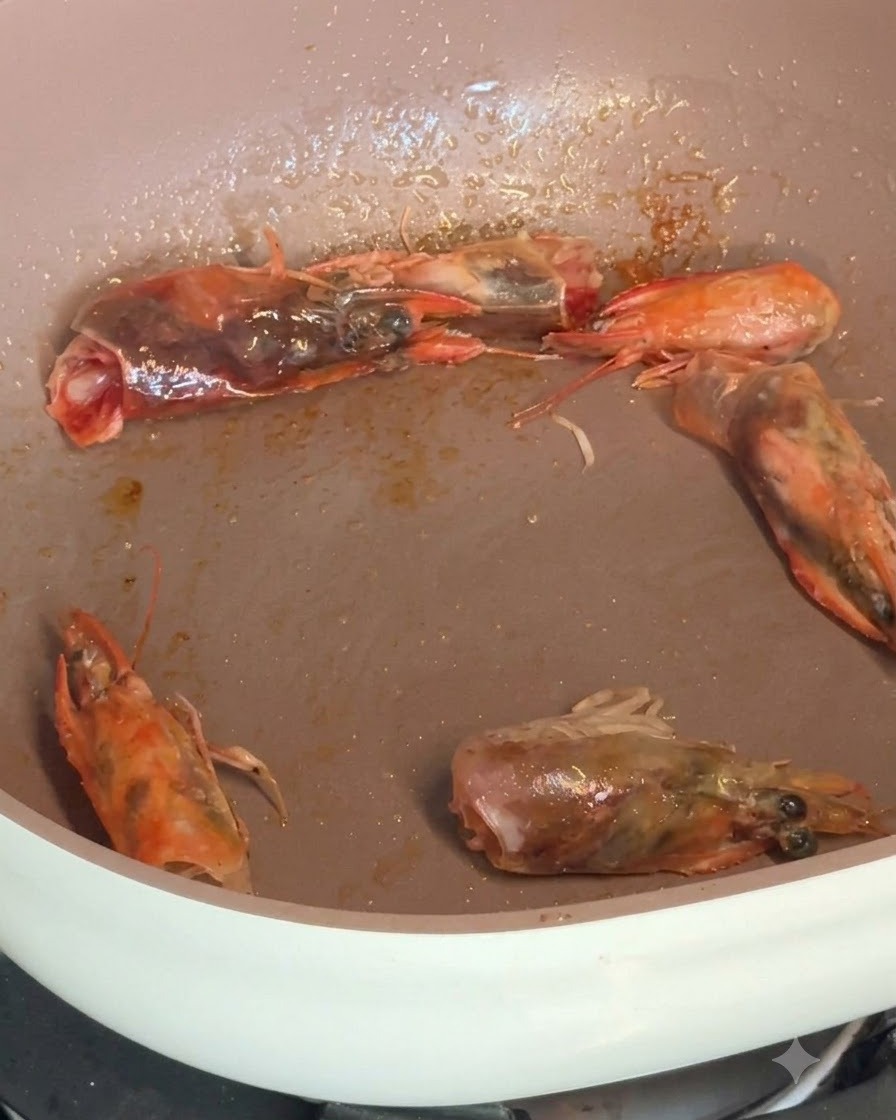 팬에서 양념과 함께 지글지글 익어가고 있는 껍질 벗긴 새우와 새우 머리.