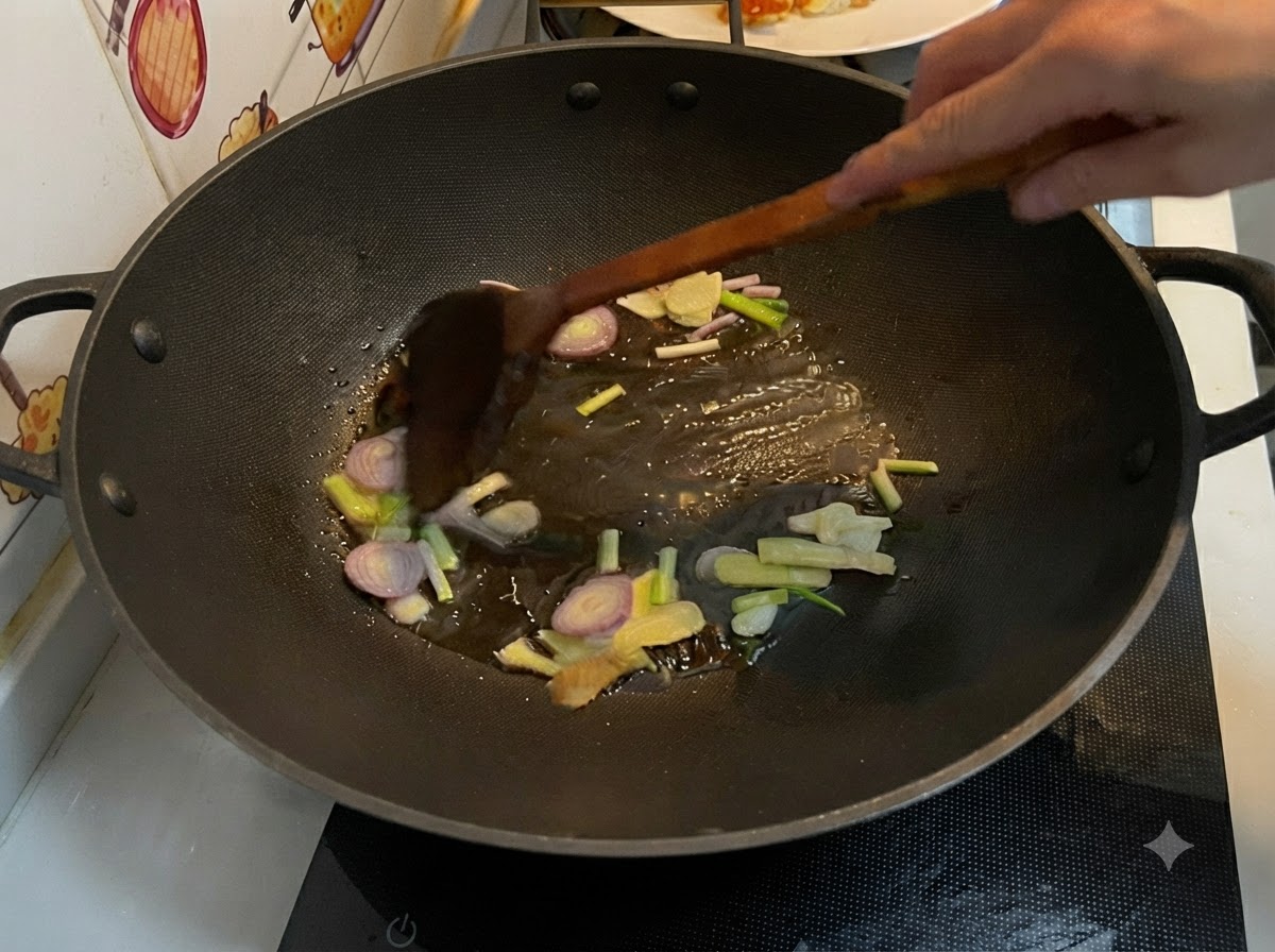 웍 안의 뜨거운 기름에서 편으로 썬 생강, 마늘, 샬롯, 쪽파를 나무 주걱으로 볶는 모습.