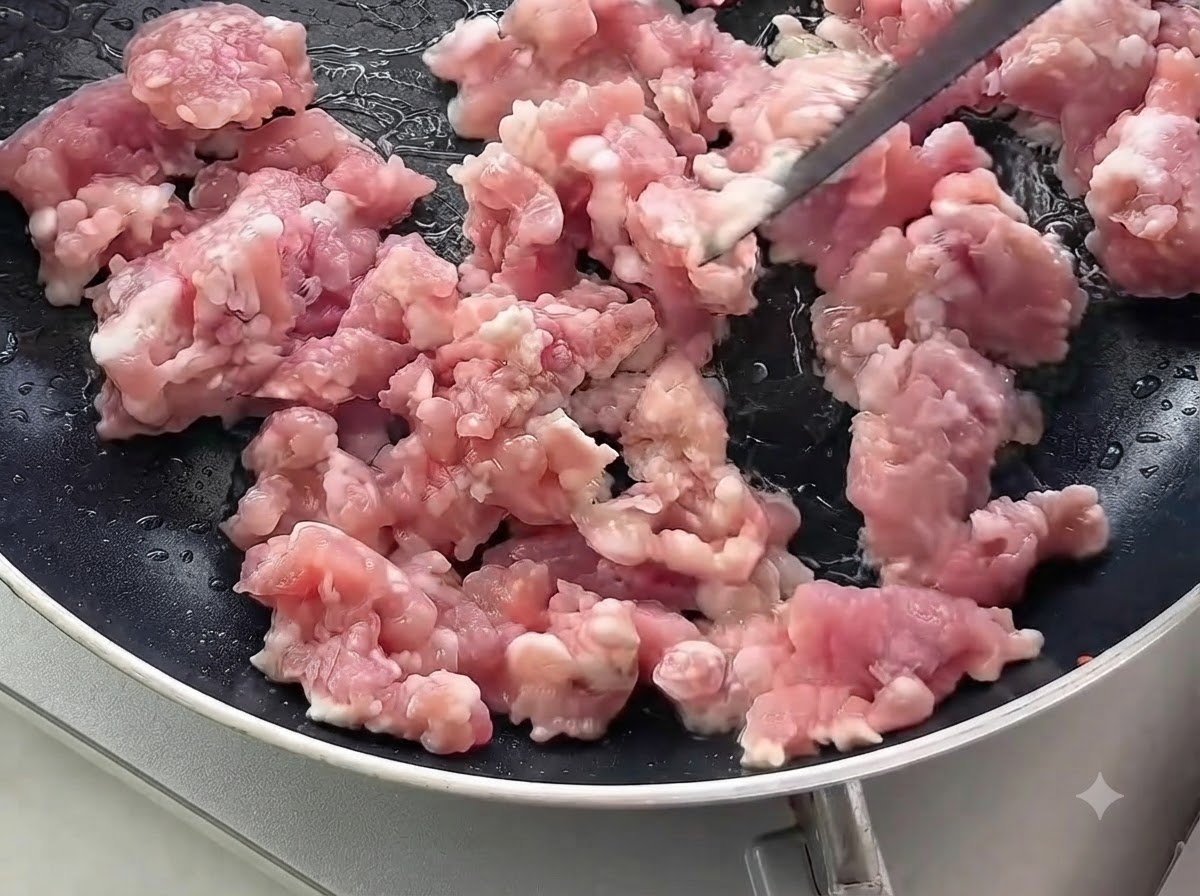 검은색 프라이팬에서 생 다진 돼지고기를 볶고 있는 모습.