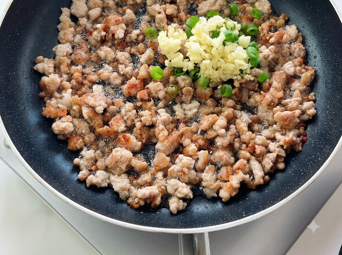 익힌 다진 고기 위에 다진 마늘과 파가 수북이 쌓여 있는 프라이팬.