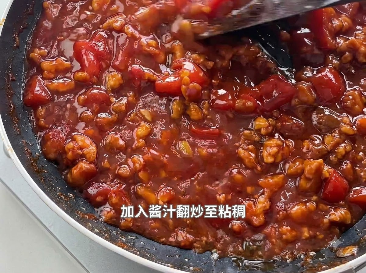 검은색 프라이팬에서 보글보글 끓고 있는 걸쭉한 토마토 고기 소스를 주걱으로 젓는 모습.