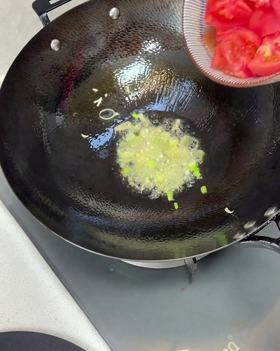 볼에 담겨 있던 썬 토마토 조각들이 향긋한 파기름이 끓고 있는 웍 안으로 쏟아져 들어가는 모습.
